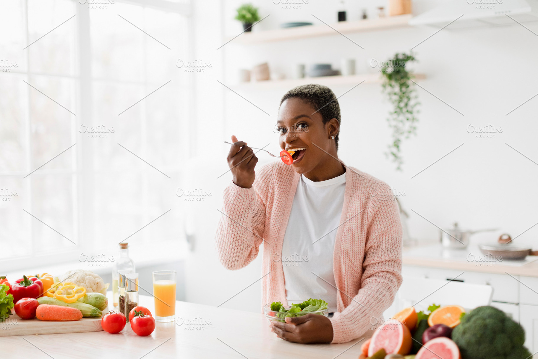 Cheerful millennial pretty black female eating salad at table with organic frui, a Person Photo by Prostock-Studio