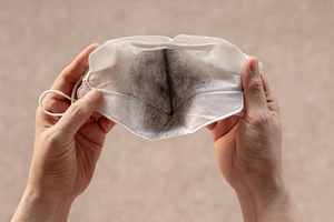 Hands holding dirty white face mask with black dust stain, pollu, a Photo by salmon.black