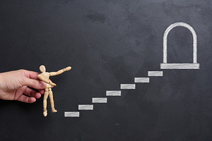 A woman's hand places a wooden mannequin on a chalk-drawn stairc, a Business Photo by ndanko