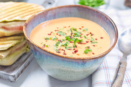 Bowl with Red bell pepper creamy soup served with grilled turkey panini, horizo