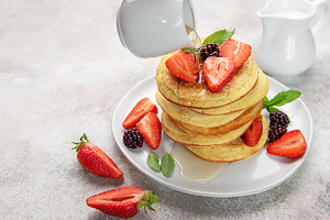 Pouring syrup over homemade pancakes with fresh berries, a Food & Drink Photo by Olena Rudo