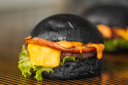 Black Beef burger filled with cheese and vegetables placed on a wooden table, a Food & Drink Photo by Half Production