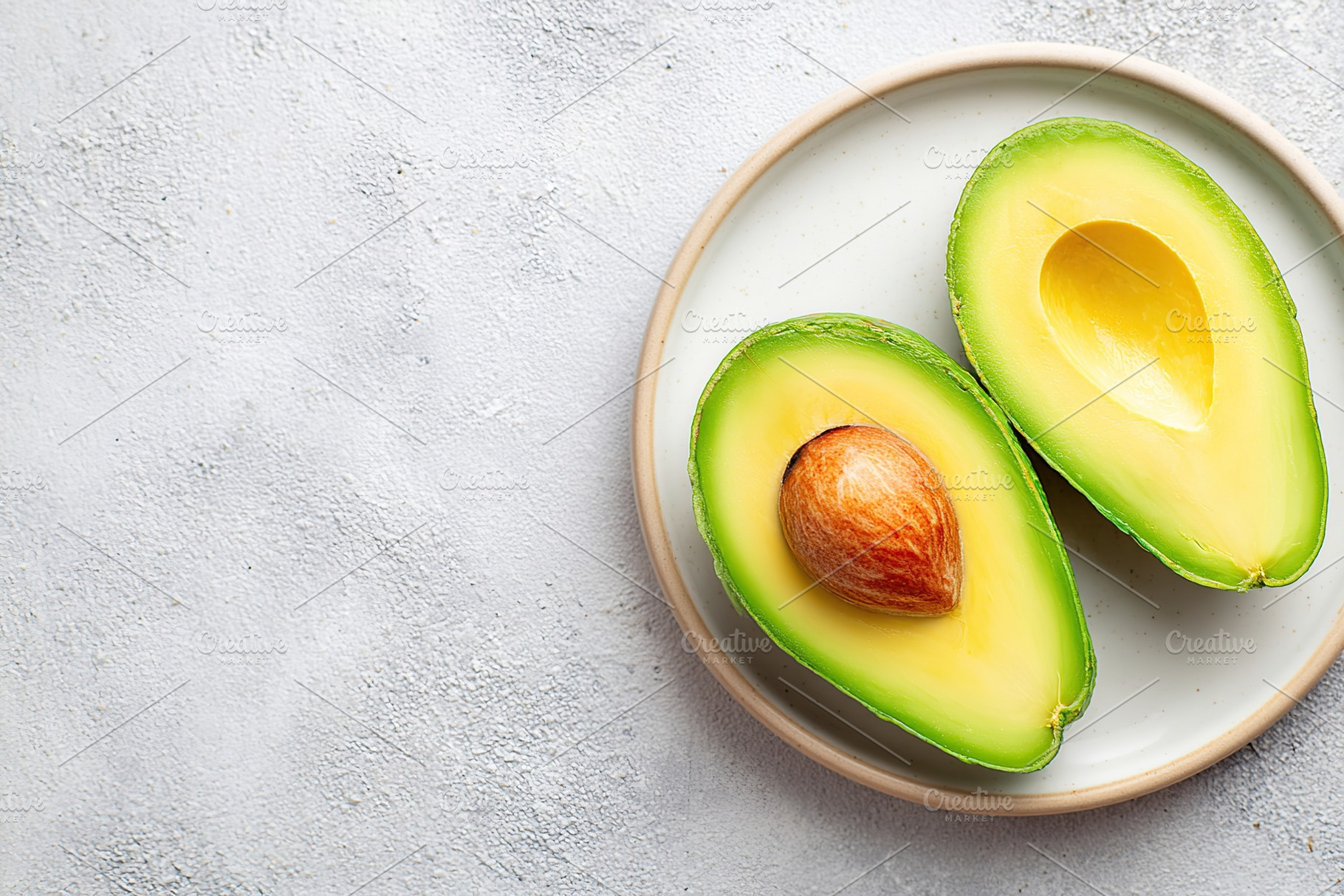 Fresh avocado halves with seed displayed on a modern white plate, a Food & Drink Photo by AlyaAnd