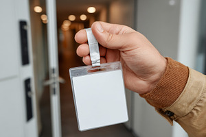 Close-up of a hand holding a blank ID badge in a modern office entrance., a Business Photo by ImageMir