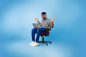 Excited young black man sitting on chair with laptop, celebrating success or ac, a Photo by Prostock-Studio