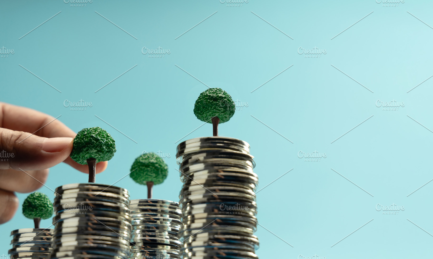 Hand putting Mini trees to growing on coin stacks symbolizing su, a Photo by salmon.black