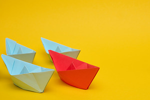 A red paper boat leads a group of three blue boats against a bri, an Abstract Photo by ndanko