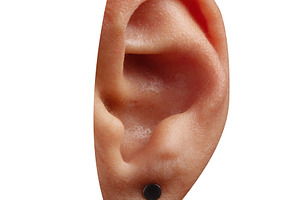 Isolated human ear wearing a small black stud earring on a white, a Person Photo by Ales Munt