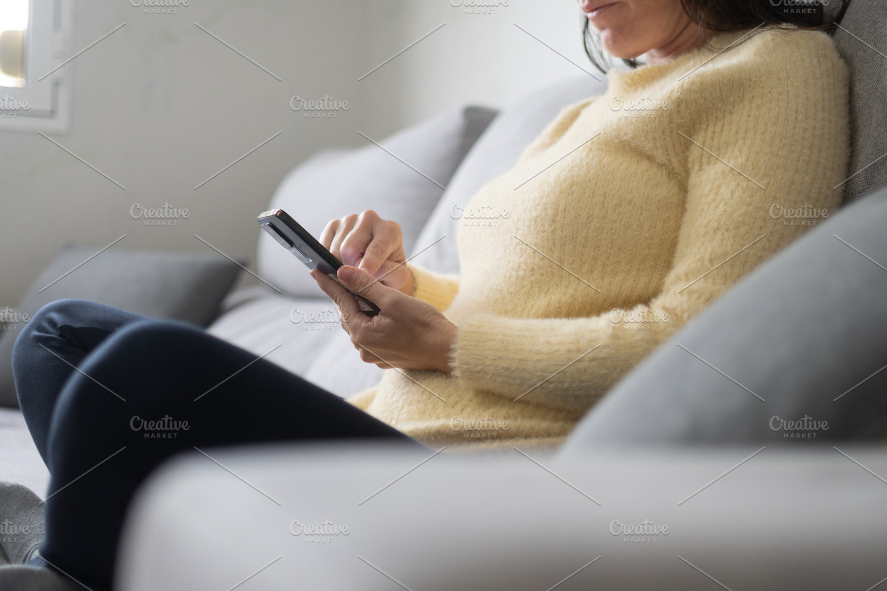 Woman using smartphone while relaxing on sofa at home in natural light, a Person Photo by etorres69