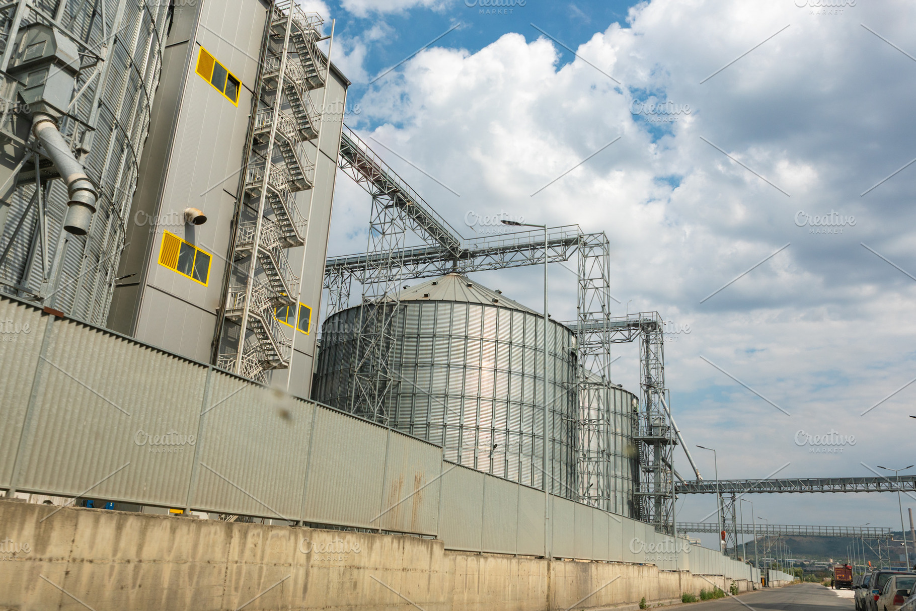 Large metal silos and industrial buildings under a partly cloudy sky, showcasin, an Industrial Photo by Ales Munt