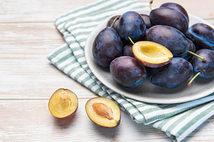 Fresh ripe plums in grey bowl on wood table, a Food & Drink Photo by Olena Rudo