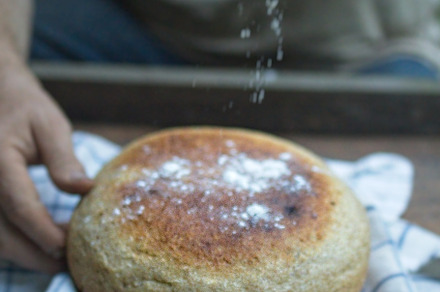 Baker's hand sprinkles flour on fresh bread close-up. A man finishes baking, de