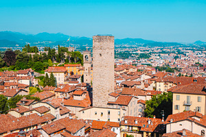a medieval stone tower among rooftops in Bergamo, a Photo by Nito