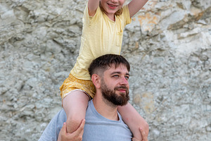Smiling father carries young daughter on shoulders outdoors, both looking happy, a Person Photo by Ales Munt