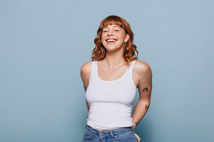 Cheerful young woman smiling at the camera while standing in a t, a Person Photo by Jacob Lund