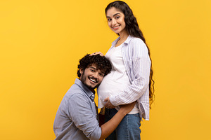 Caring indian man putting his ear on wife's pregnant tummy, listening to baby's, a Photo by Prostock-Studio