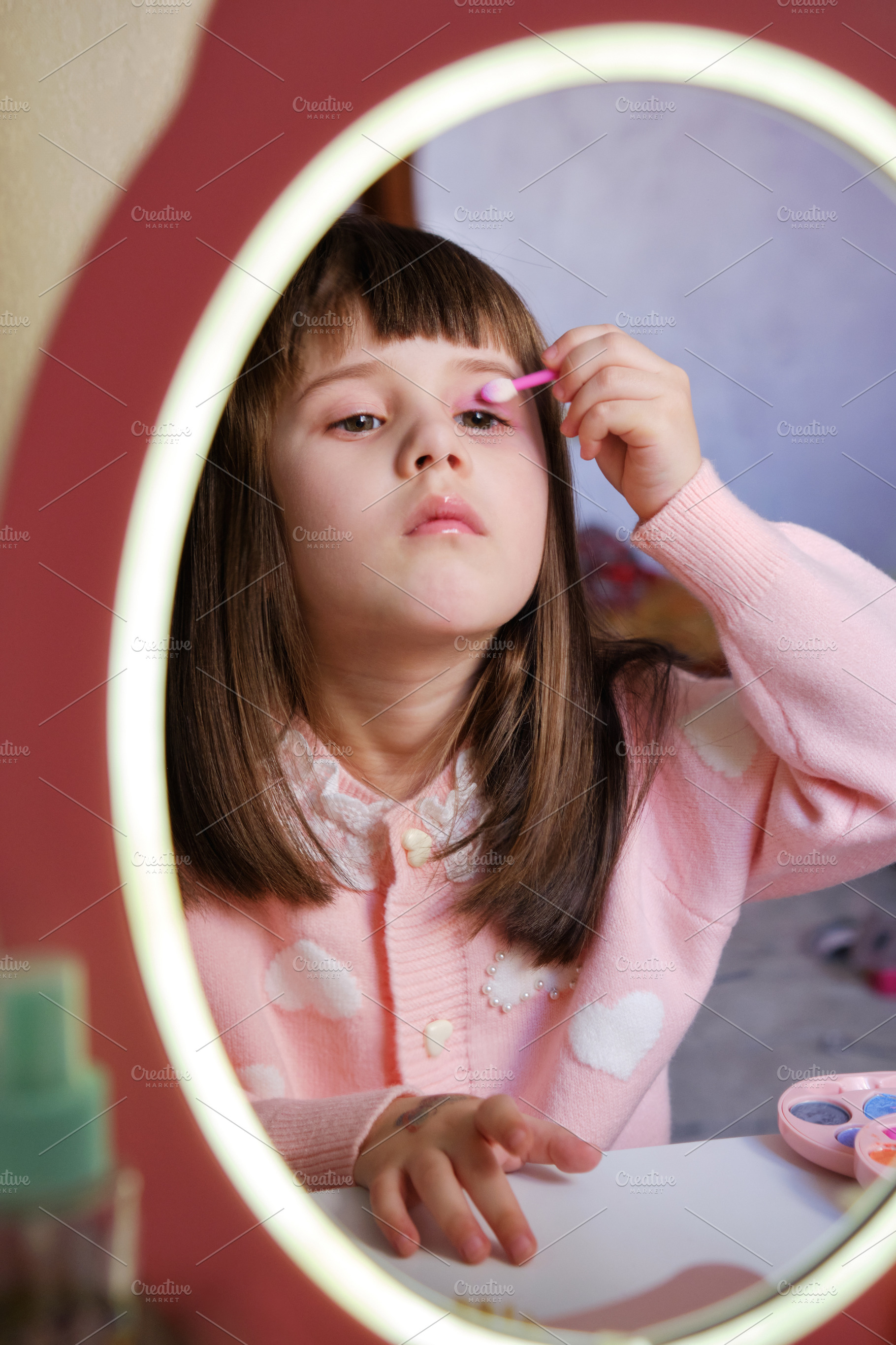 Little girl pretending to apply eye shadow looking in a toy vanity mirror., a Person Photo by Rohan Photography