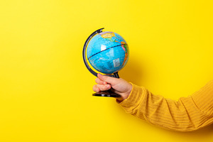 Close-up of a hand in a yellow sleeve holding a small globe agai, a School & Education Photo by Ales Munt