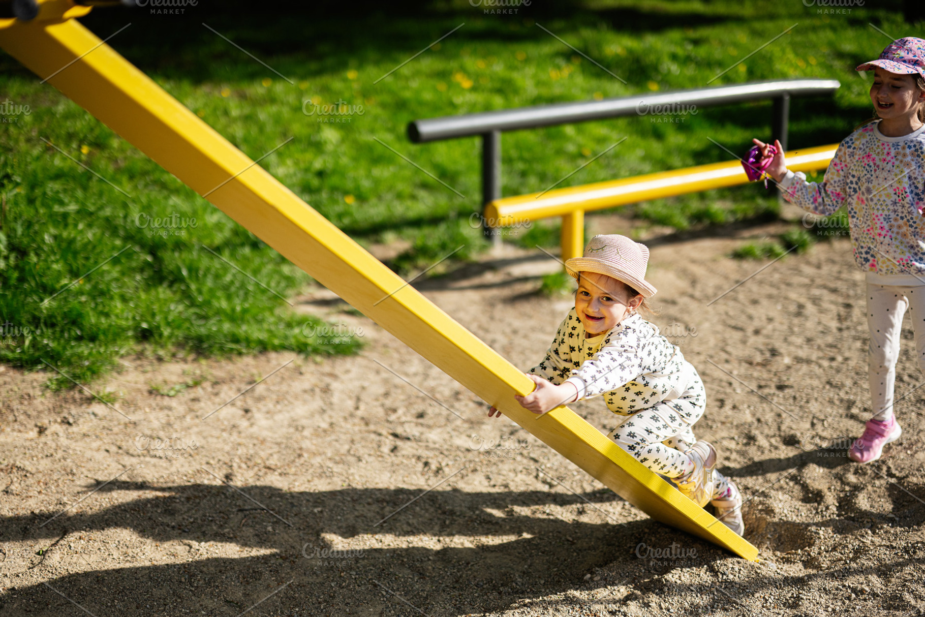 Children playing together on a yellow seesaw in a sunny playground, a Person Photo by AS photostudio