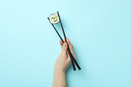 Female hand holding maki with chopsticks on blue background, a Food & Drink Photo by AtlasStudio