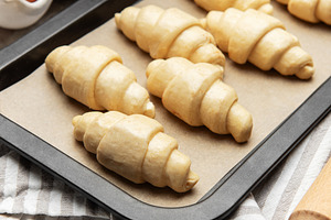 Freshly made croissants resting on baking sheet await oven's war, a Food & Drink Photo by Olena Rudo