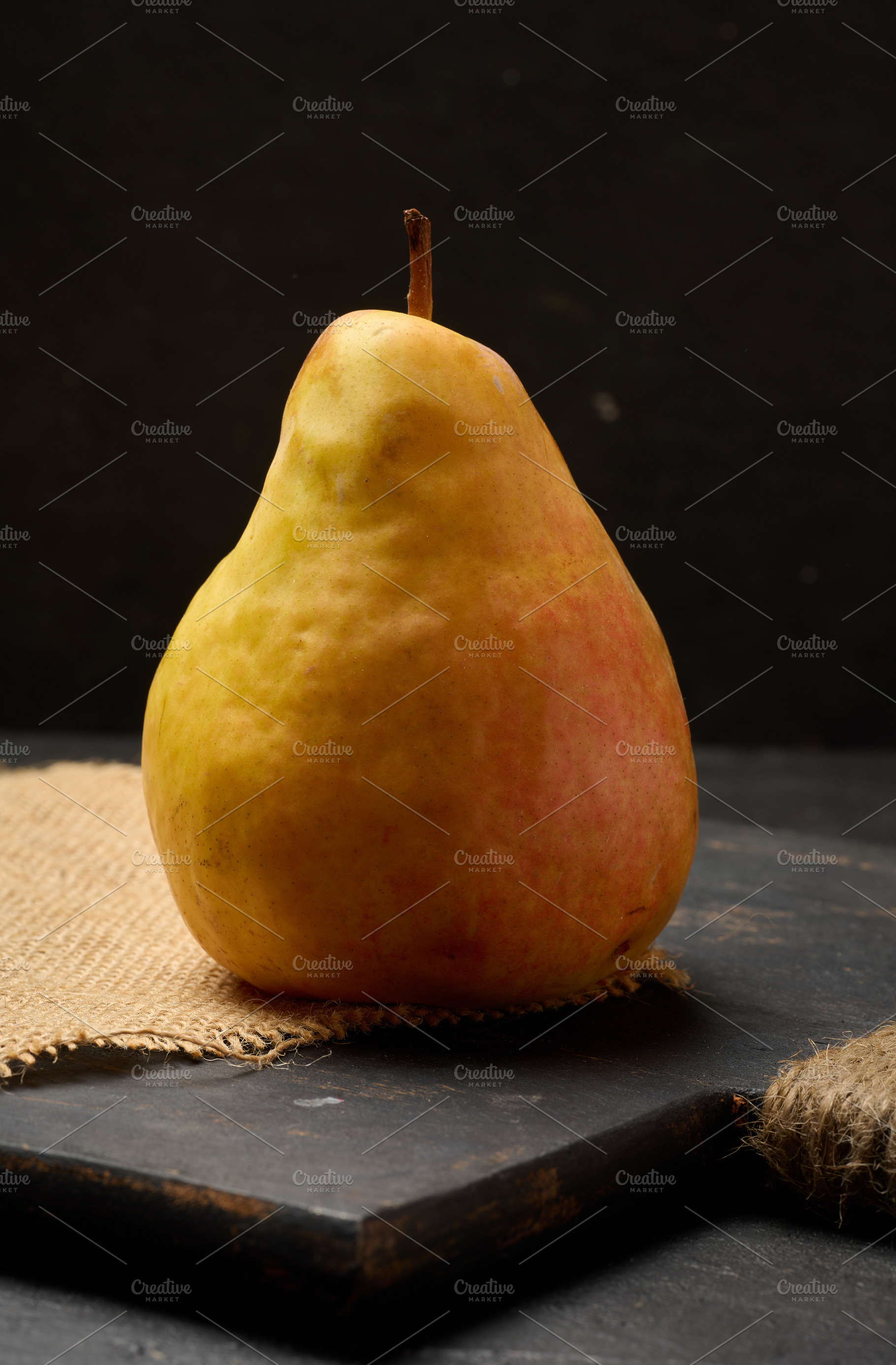 A ripe yellow pear with its stem, on a dark wooden board, a Food & Drink Photo by ndanko
