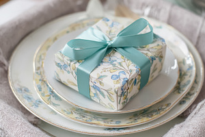 Wrapped gift box with a teal ribbon bow sitting on floral patter, a Photo by Studio ANNA