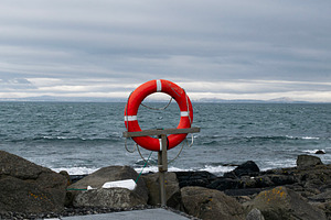 Lifesaver on a rock-lined coast in Akranes, Iceland under a cloudy sky, a Photo by AS photostudio