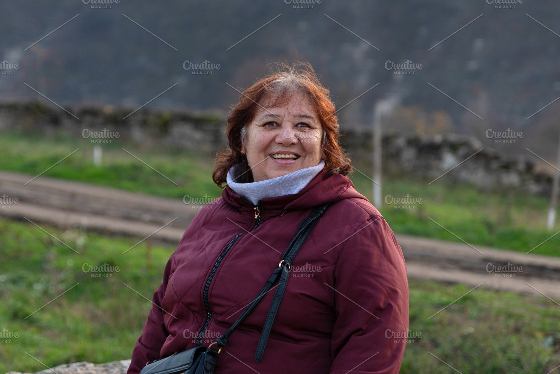 Happy older woman in a maroon jacket smiling outdoors with a nat, a Person Photo by Ales Munt