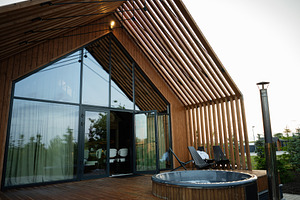 Modern wooden house facade with outdoor hot tub and patio seating area, a Photo by AS photostudio