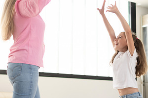 Happy mother and daughter playing together with raised arms at home, a Person Photo by etorres69