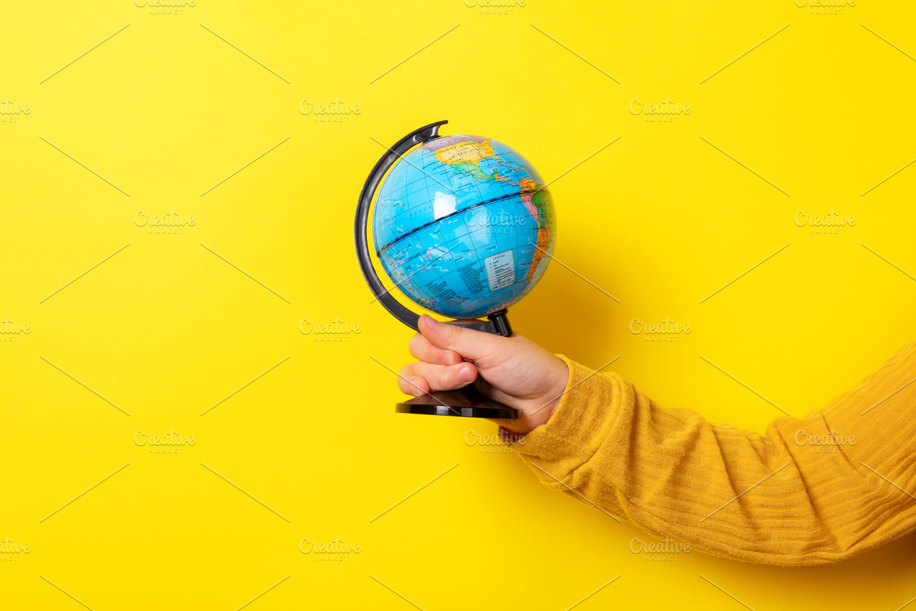 Close-up of a hand in a yellow sleeve holding a small globe agai, a School & Education Photo by Ales Munt