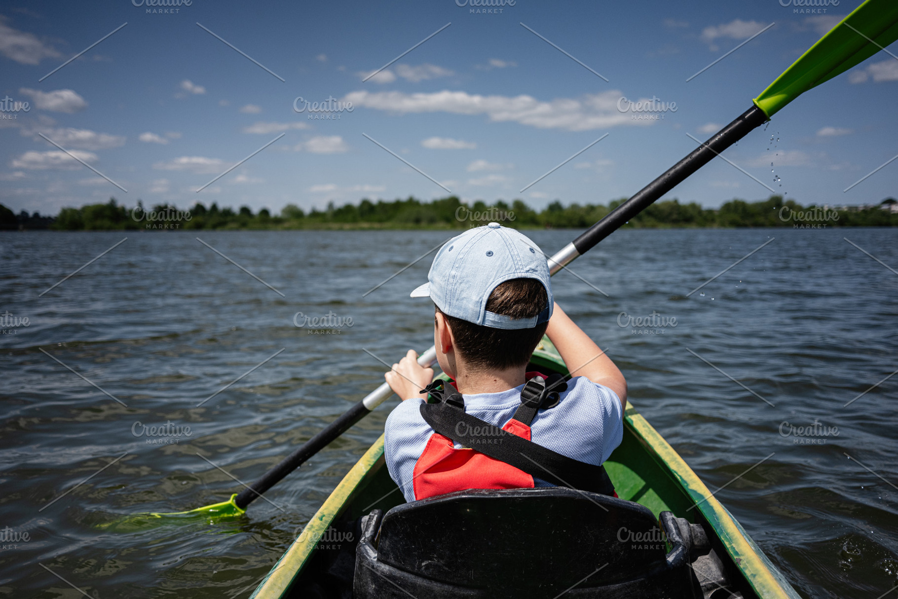 Child kayaking in calm lake water under a sunny blue sky, a Photo by AS photostudio