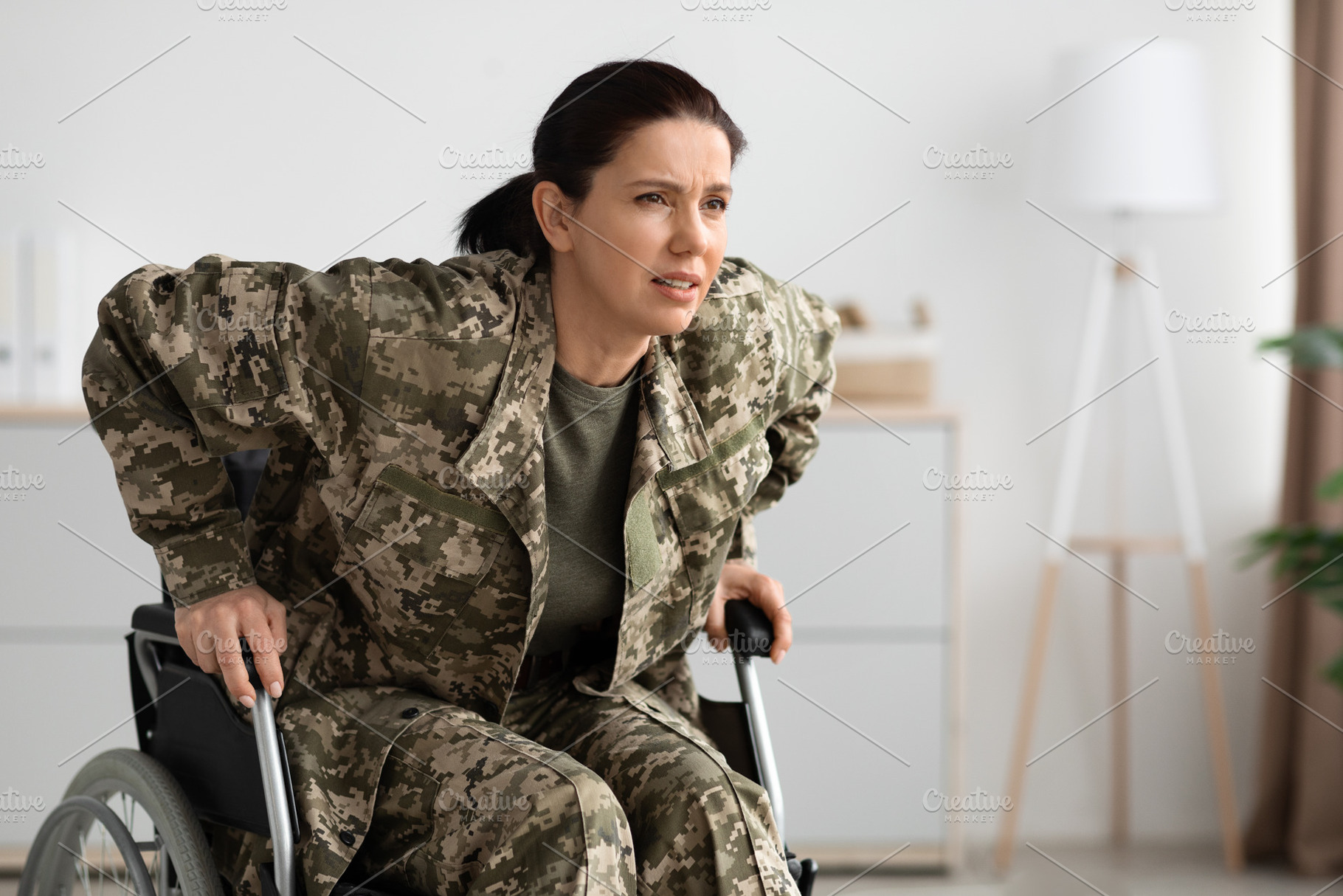 Paraplegics Concept. Soldier Woman Trying To Get Up From Wheelchair At Home, a Photo by Prostock-Studio