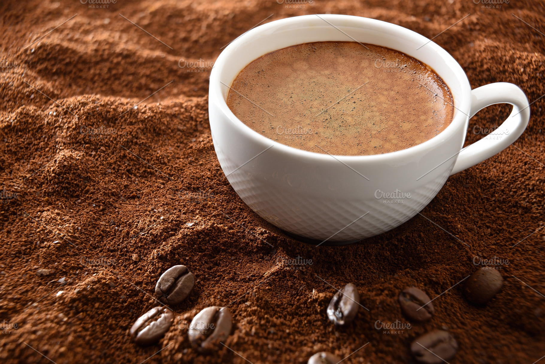 Cup of frothy coffee over ground with beans elevated view, a Food & Drink Photo by Davizro's Market