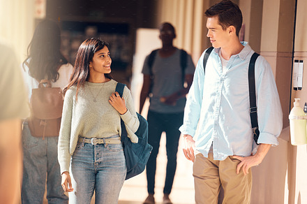 Students, man or woman walking in hallway of school, university or college campus for education, global learning or study bonding. Smile, happy or scholarship friends talking and future success goals, a Photo by Peopleimages.com