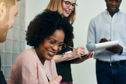 Smiling african businesswoman working with colleagues in an office stock, a Business Photo by Stefan & Janni