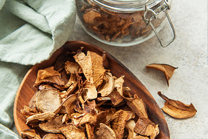 Dried mushrooms on wooden plate with fresh mushrooms and jar, a Food & Drink Photo by Olena Rudo