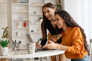 Two Happy Ladies Using Laptop Computer Working Online In Office, a Photo by Prostock-Studio