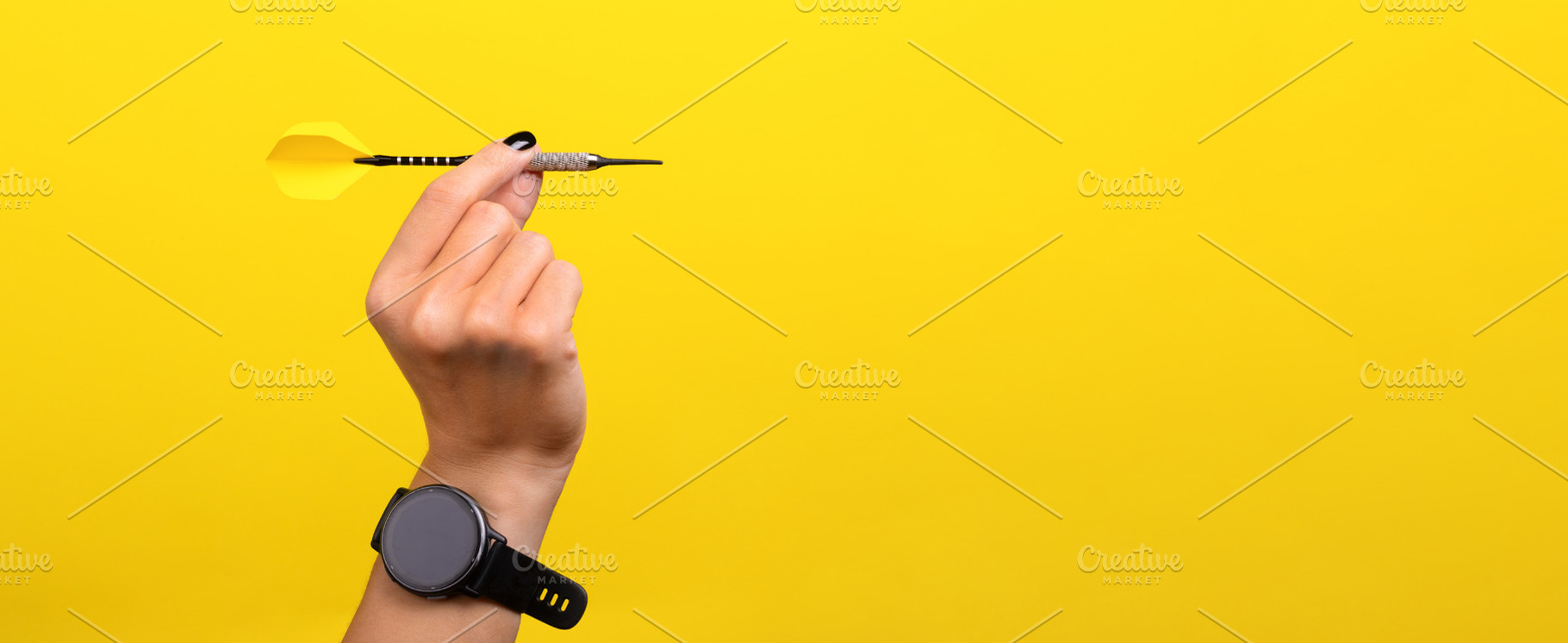 Close-up of a hand holding a dart against a bright yellow backgr, a Sports & Recreation Photo by Ales Munt