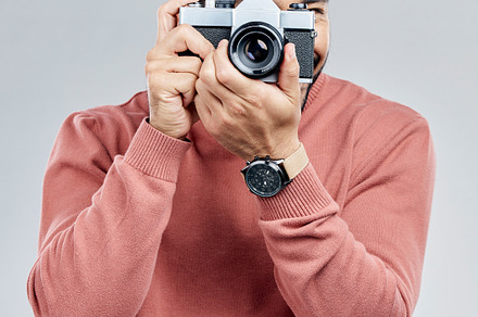 Man with camera, photography and artist, taking picture with art isolated on gray background. Photographer, focus with lens and creativity with vintage technology and creative male in studio, a Photo by Peopleimages.com
