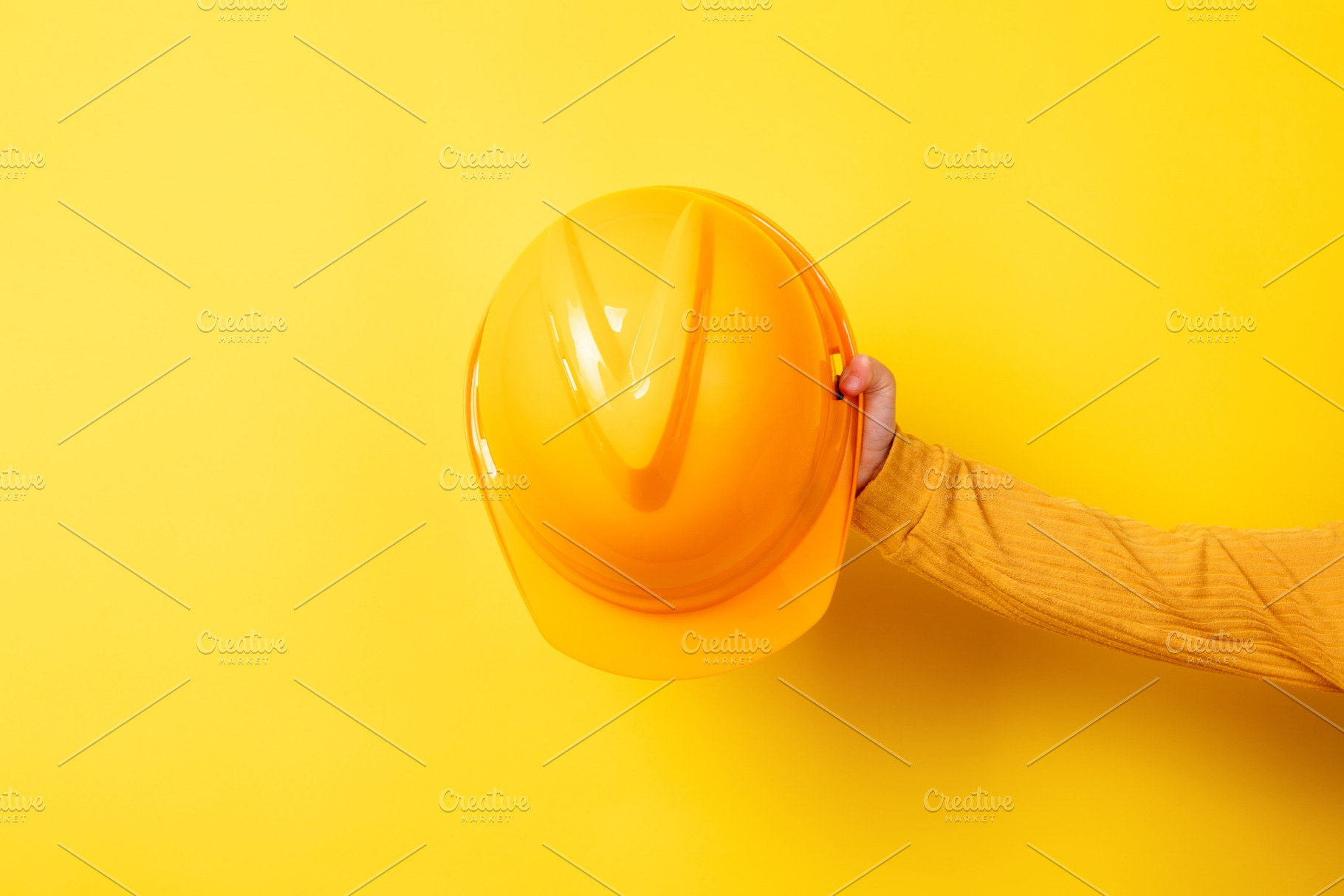 Hand holding a yellow construction helmet against a matching yel, an Industrial Photo by Ales Munt
