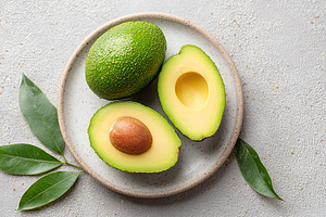 Freshly cut avocado halves with seed displayed on modern white plate with green, a Food & Drink Photo by AlyaAnd