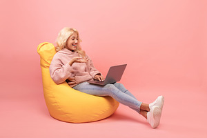 Happy woman relaxing in beanbag chair with laptop, female student using modern, a Photo by Prostock-Studio