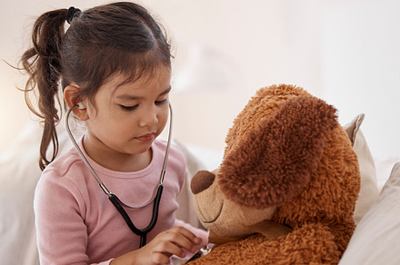 Stethoscope, little girl and a teddy bear. cute adorable Asian child dreams of becoming a doctor, holing a stethoscope, pretending to be checking a teddy bear's temperature at home., a Photo by Peopleimages.com