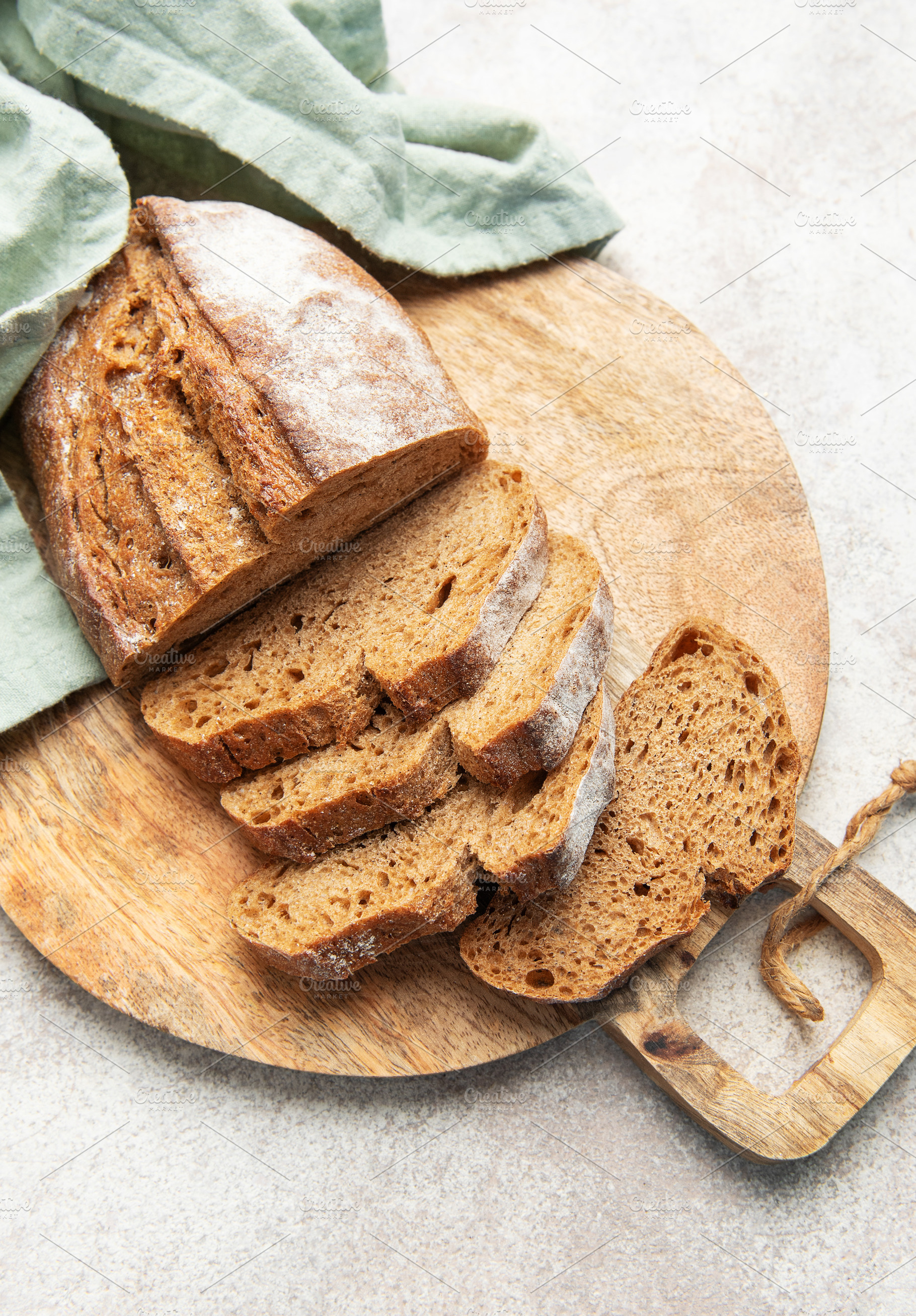 Slicing fresh whole grain rye bread on wooden board, a Food & Drink Photo by Olena Rudo