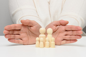 Female hands protect wooden figures of a family of parents and t, a Person Photo by ndanko