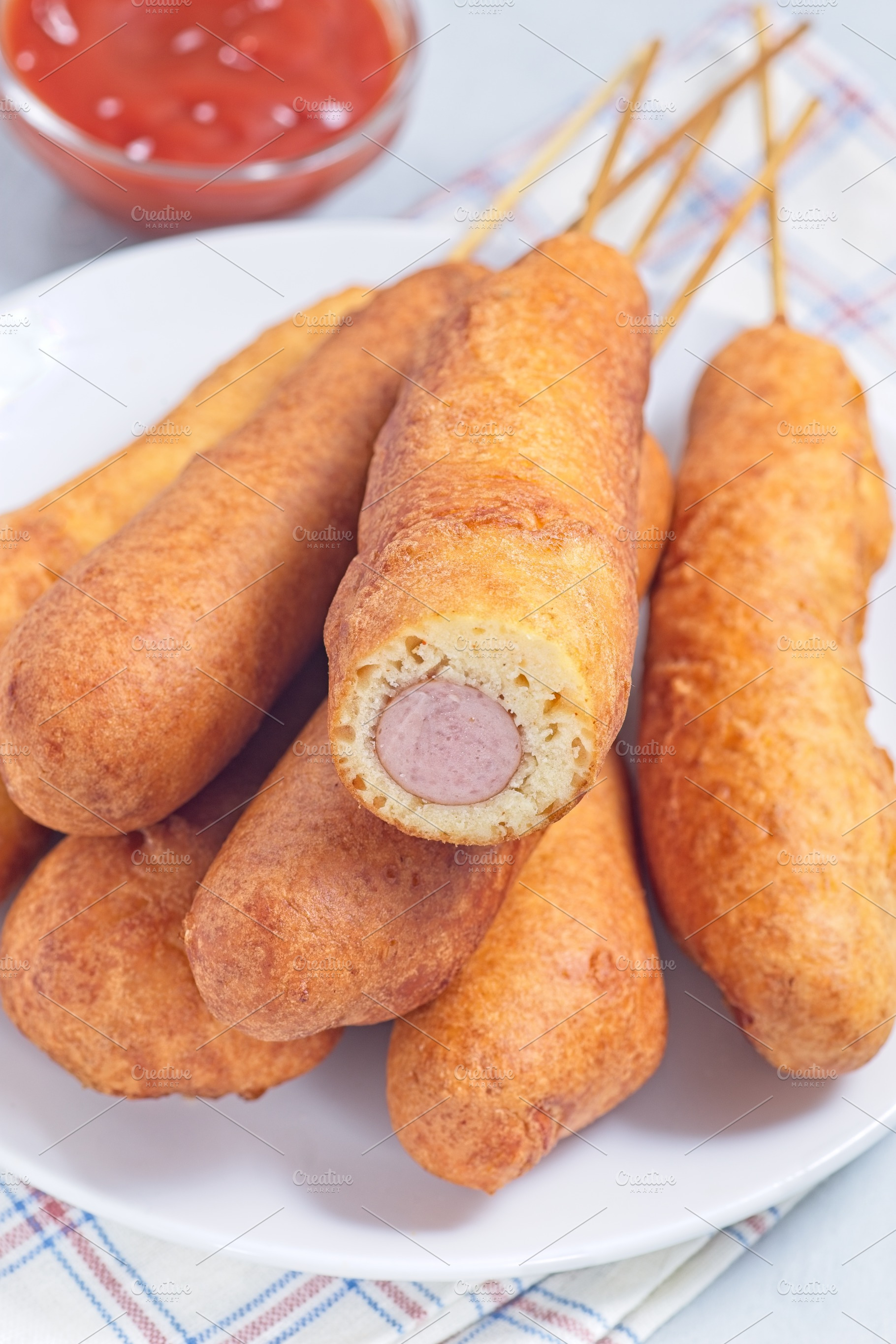 Heap of corn dogs on white plate, served with ketchup, vertical closeup, a Food & Drink Photo by iuliia_n