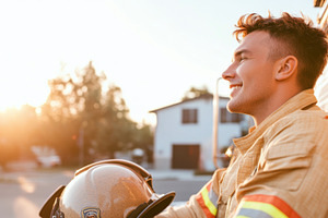 Smiling firefighter in uniform holding helmet outside, bright su, a Photo by Dvoevnore photos