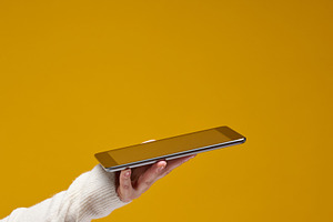 Hand wearing a white sweater holds a silver tablet against a sol, a Technology Photo by ndanko